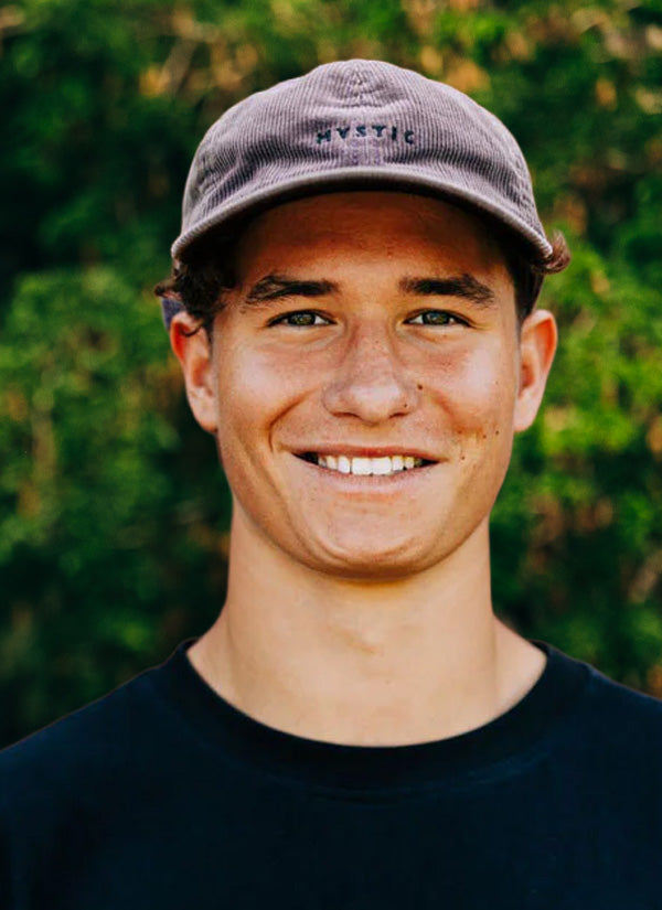 Nils R team headshot, smiling, wearing a cap with blurred trees in the background