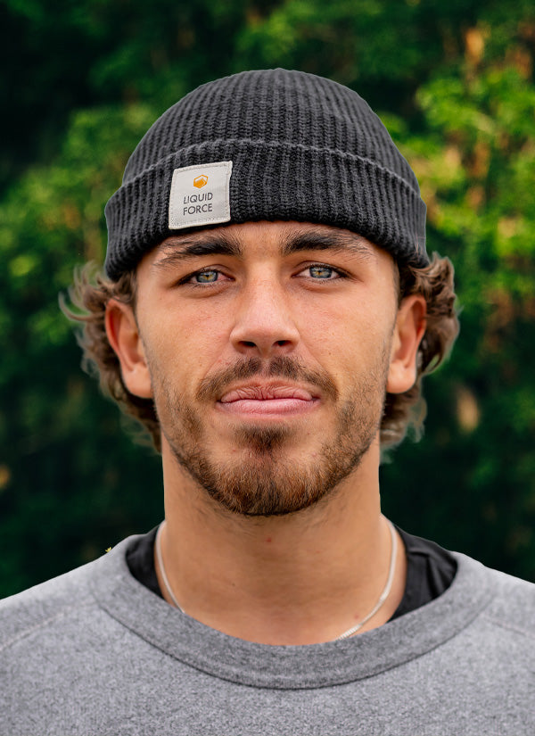 Rudy T team headshot wearing a gray knit beanie with a LiquidForce brand logo against a blurred green background