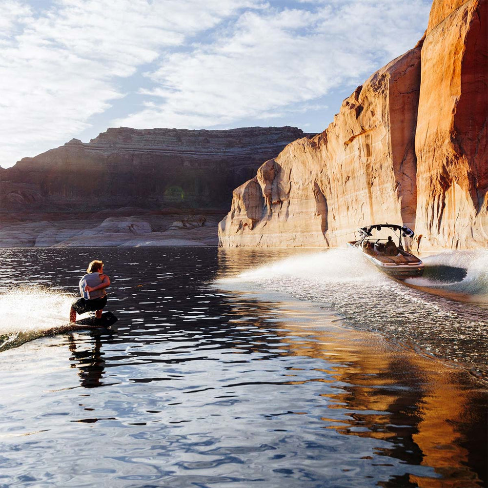 Boat speeding through water pulling Luka K on a wakeboard surrounded by large rock formations.