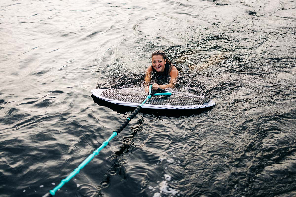 Woman in water gripping wakesurf rope and smiling at the camera.