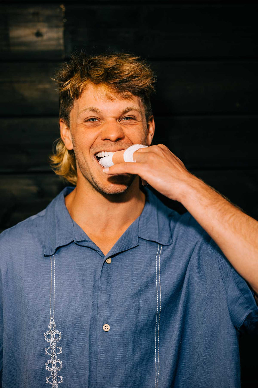 Person in a blue shirt biting a napkin while smiling happily.