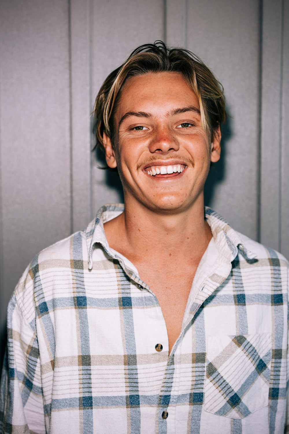 Cheerful young man with blonde hair in a plaid shirt.