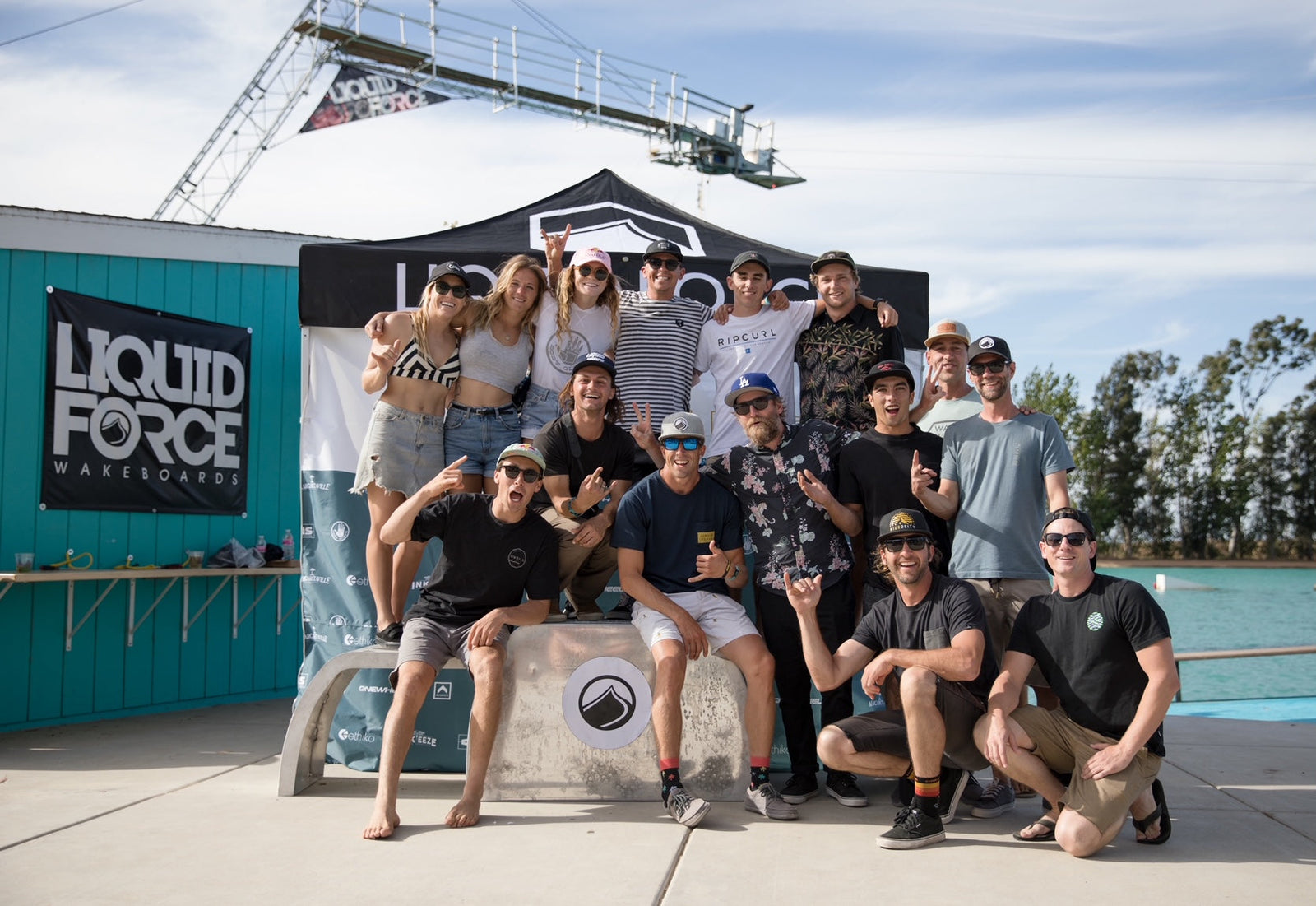 A group of smiling people pose joyfully in front of a "Liquid Force Wakeboards" banner.