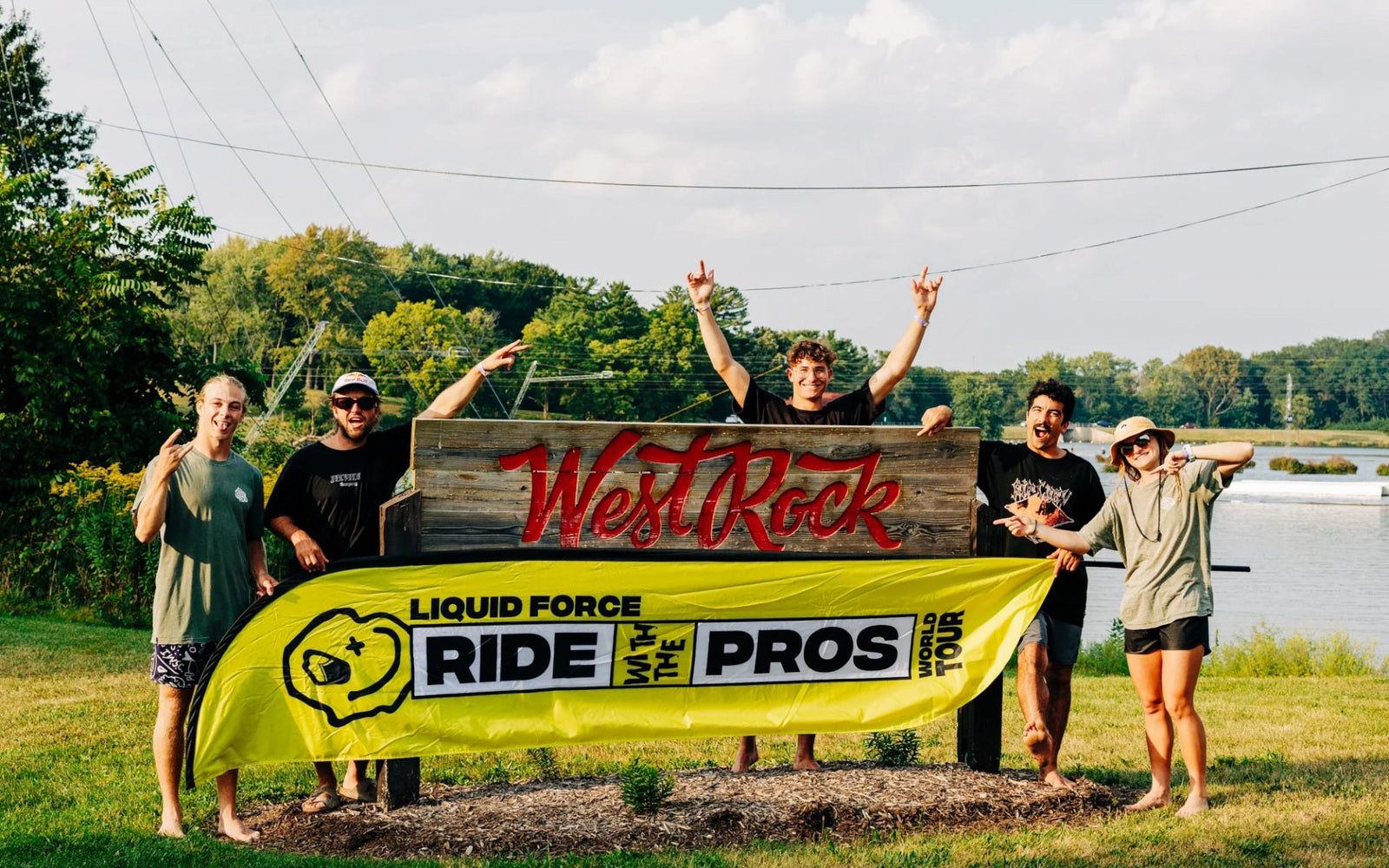 Group poses by “West Rock” sign with Liquid Force Ride With The Pros banner in grassy park.