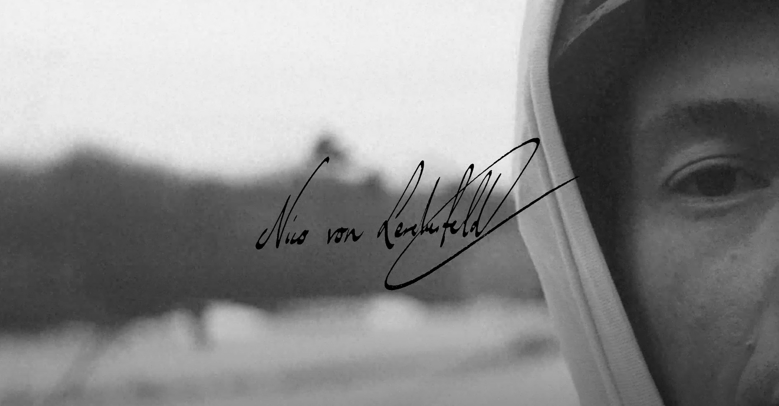 Close-up of a person’s face in black and white, wearing a hood.