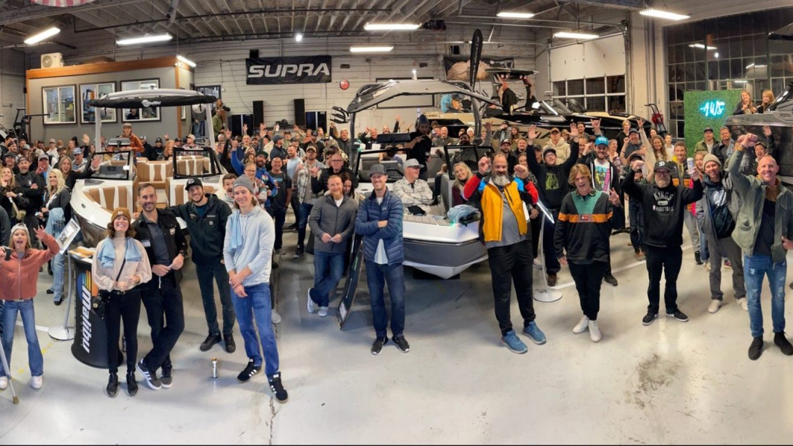 Large crowd poses around boats in a showroom during a community event at AWS.