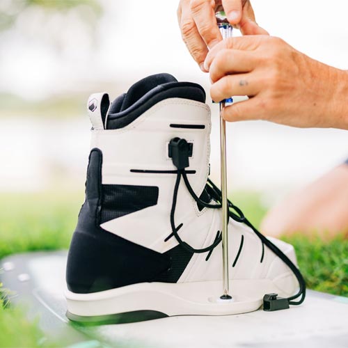 Person using screwdriver to attach white Liquid Force binding to wakeboard.