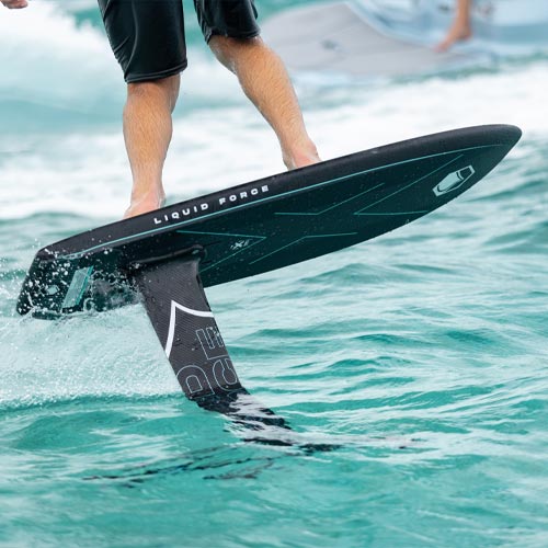 Close-up of Liquid Force foil board lifting above water with rider's legs visible.