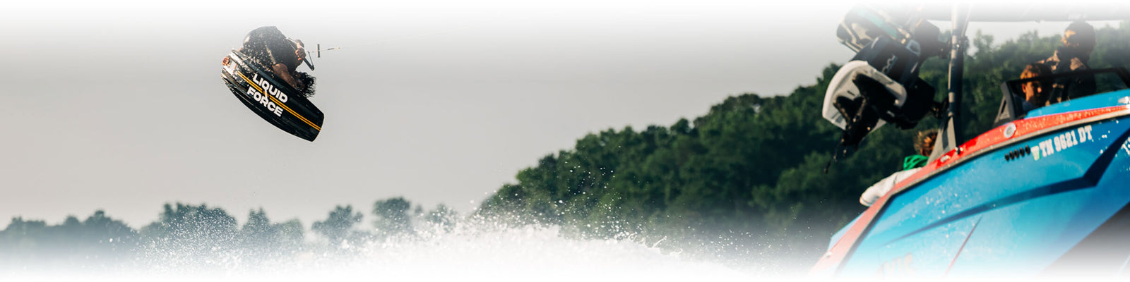 Person wakeboarding with trees and a boat in the background.