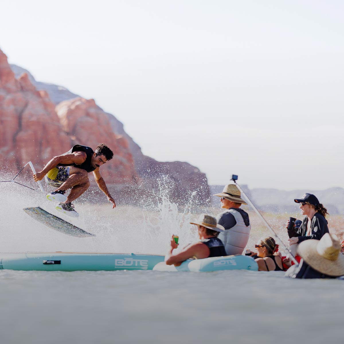 Wakeskater jumping over water float with other people watching from the water