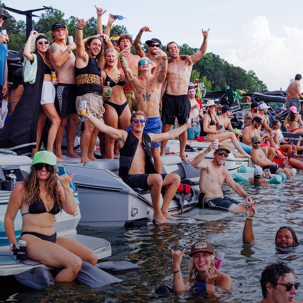 Group of people celebrating on boats gathered on lake during summer wakeboarding event.