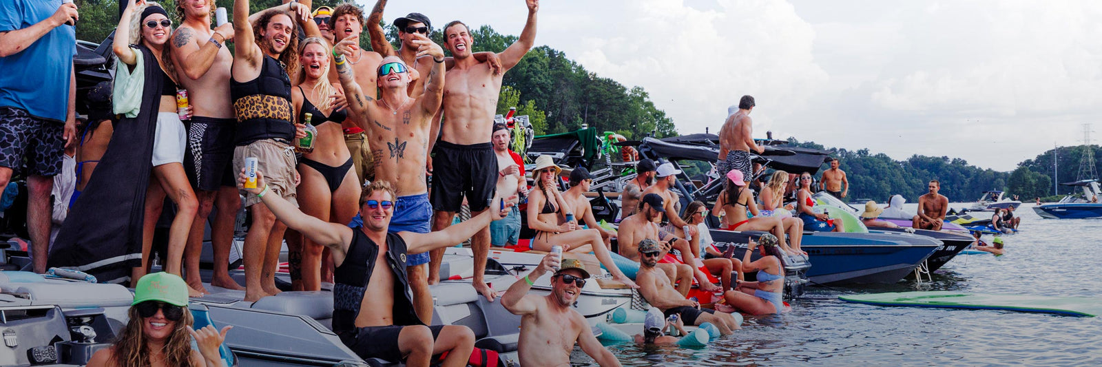 Group of people celebrating on boats gathered on lake during summer wakeboarding event.