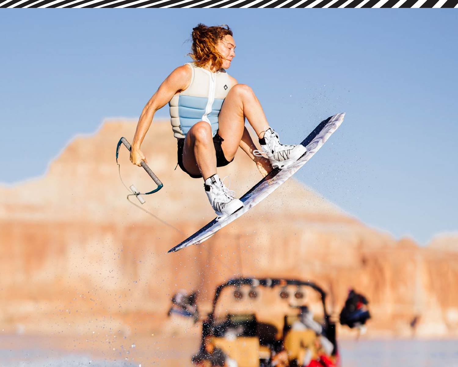 Girl wakeboarding in the air with a clear blue sky and canyons in the background