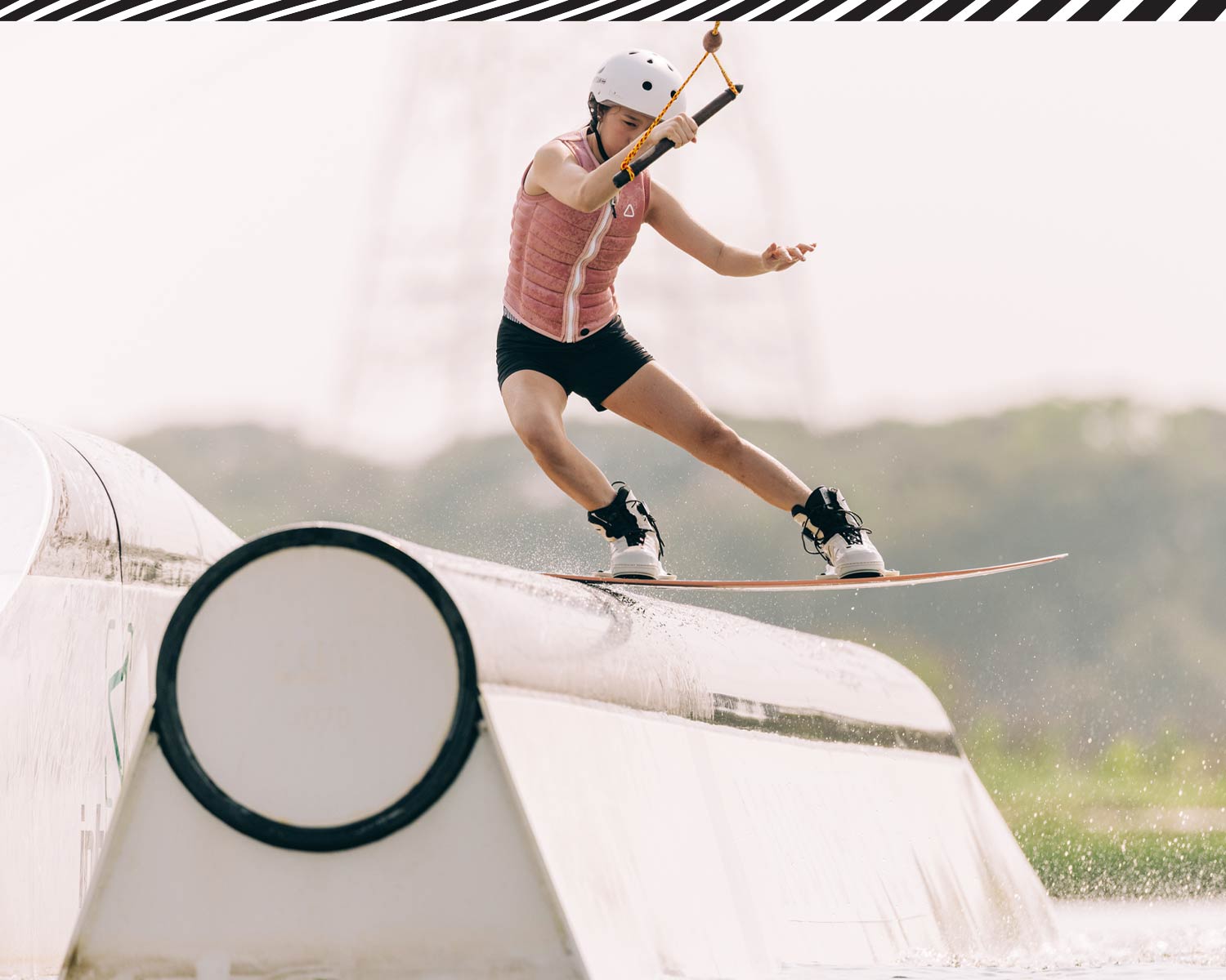 Rider sliding rail feature on wakeboard while holding handle, wearing helmet and vest.