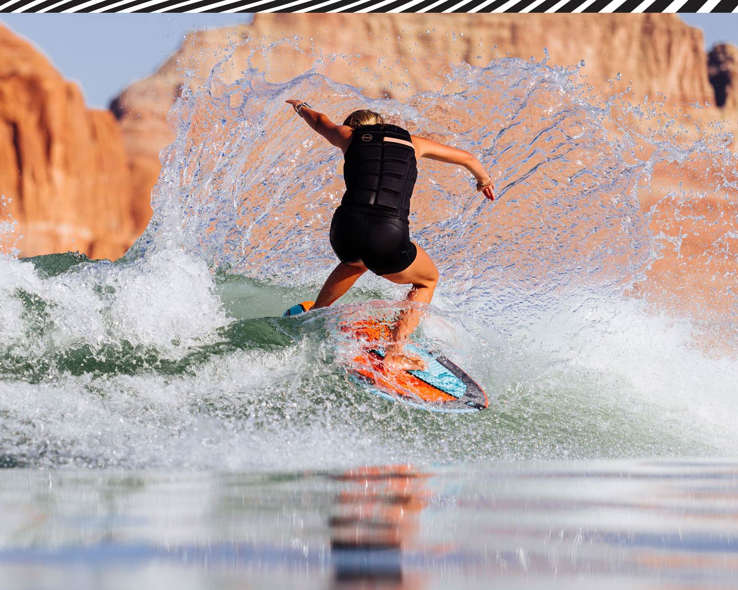 Girl wake surfing on a wave with rocky cliffs in the background