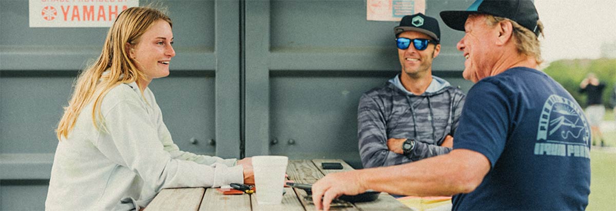 Woman smiles while talking with two men at a picnic table.