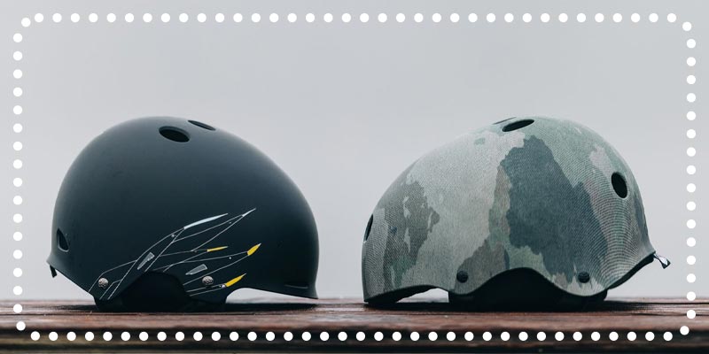 Two helmets, one matte black with arrows, the other in camo print, on a wooden surface.