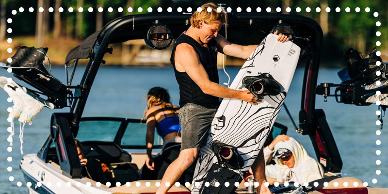 Man loading a white wakeboard with black boots onto a boat.