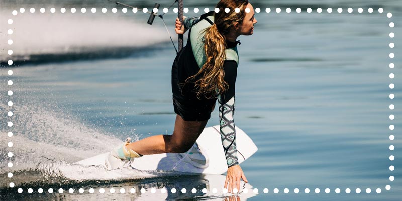 Woman wakeboarding with one hand touching the water and a handle in the other.