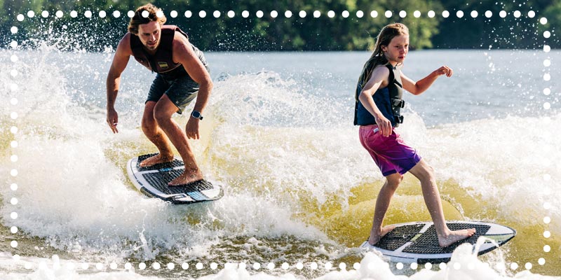 Man and girl wakesurfing together on a sunny lake.