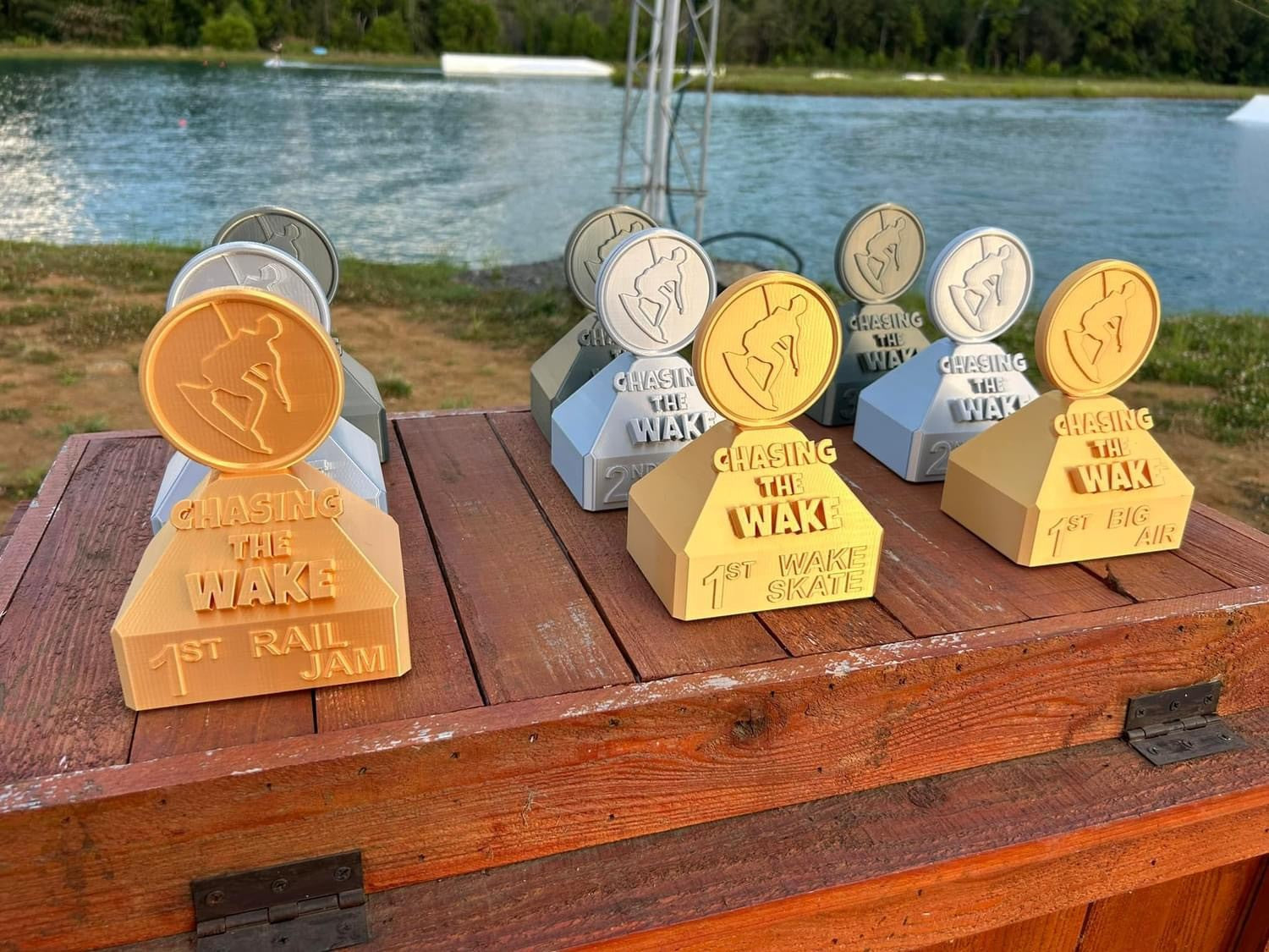 Gold and silver “Chasing the Wake” trophies sit on a wood table by a lake.