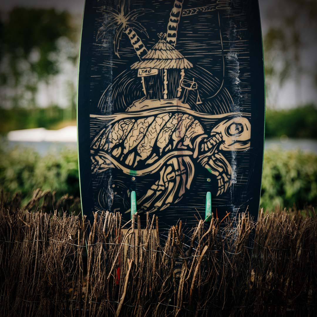 TAO Skate Nubs mounted on bottom of wakeskate with turtle and hut design lie on a dry, grassy field.