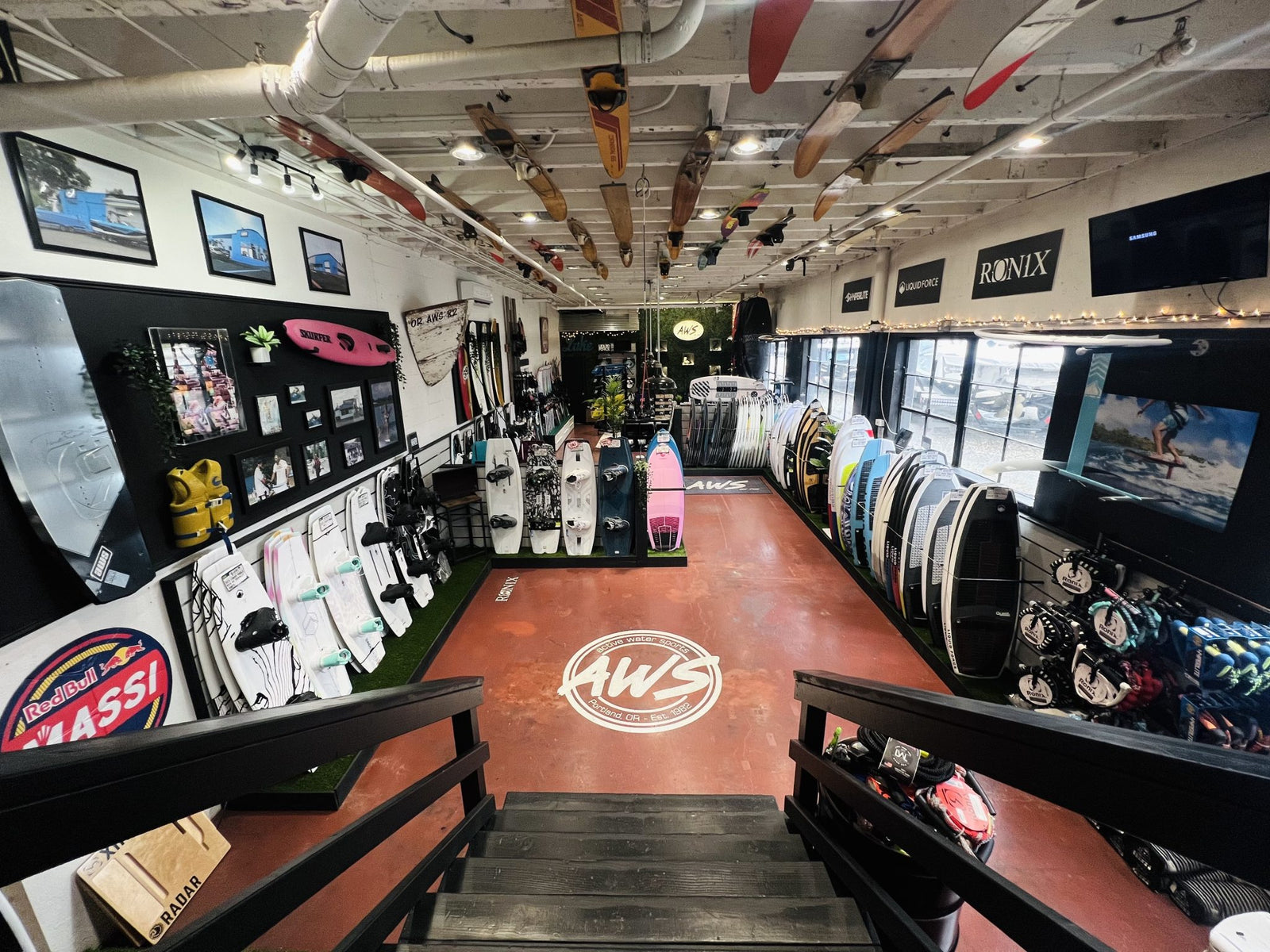 View from stairs into a watersports store lined with wakeboards, surf gear, and photos.