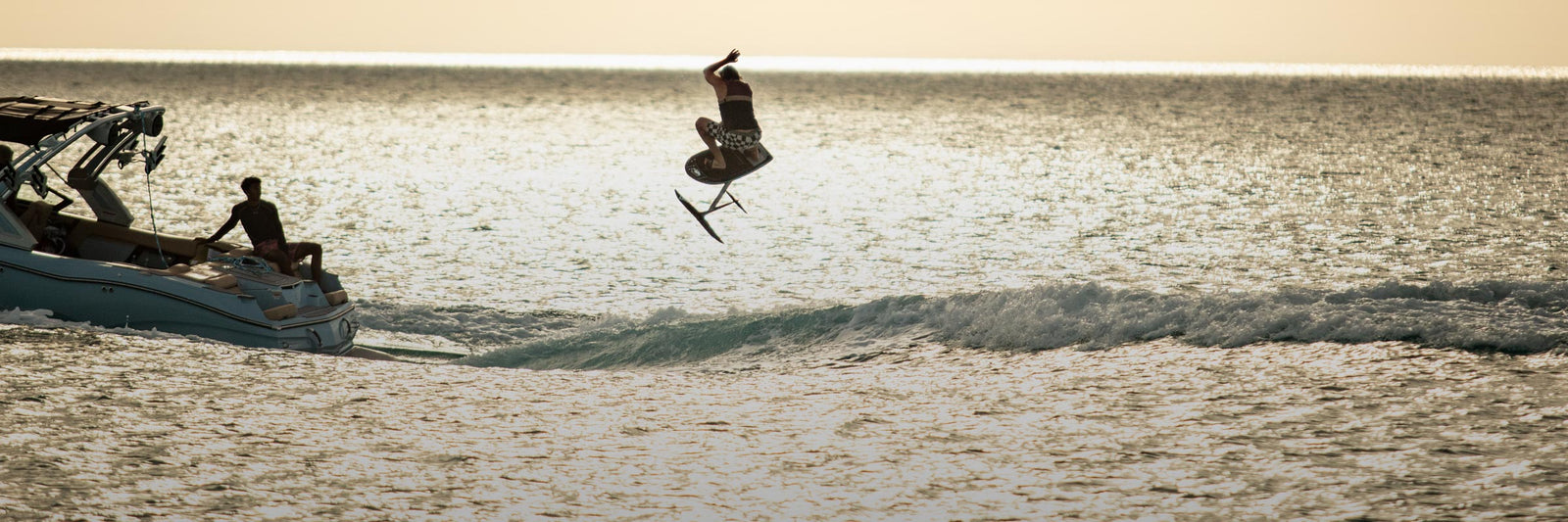 Liquid Force Foil Package Collection - Closeup shot of LF Athlete Harley Clifford doing an arial maneuver on a foil behind the boat at sunset.