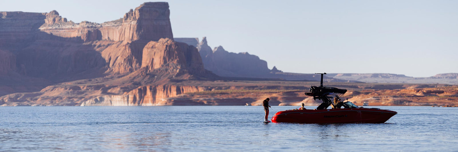 Rider standing beside a red boat on a calm lake with large desert rock formations behind.