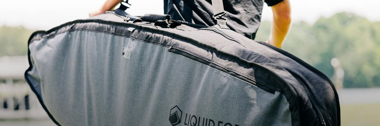 Person carries a large padded board bag with the Liquid Force logo on the side.