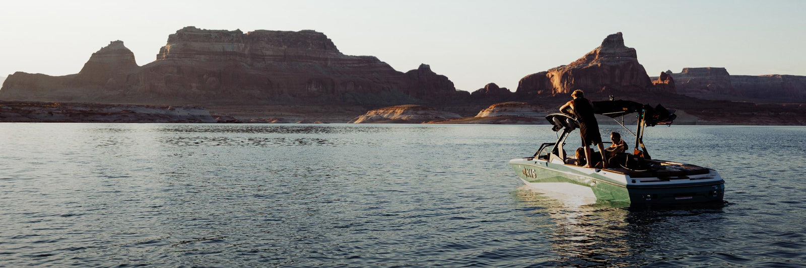 Boat with riders floats on a calm lake with large rocky cliffs in the background.
