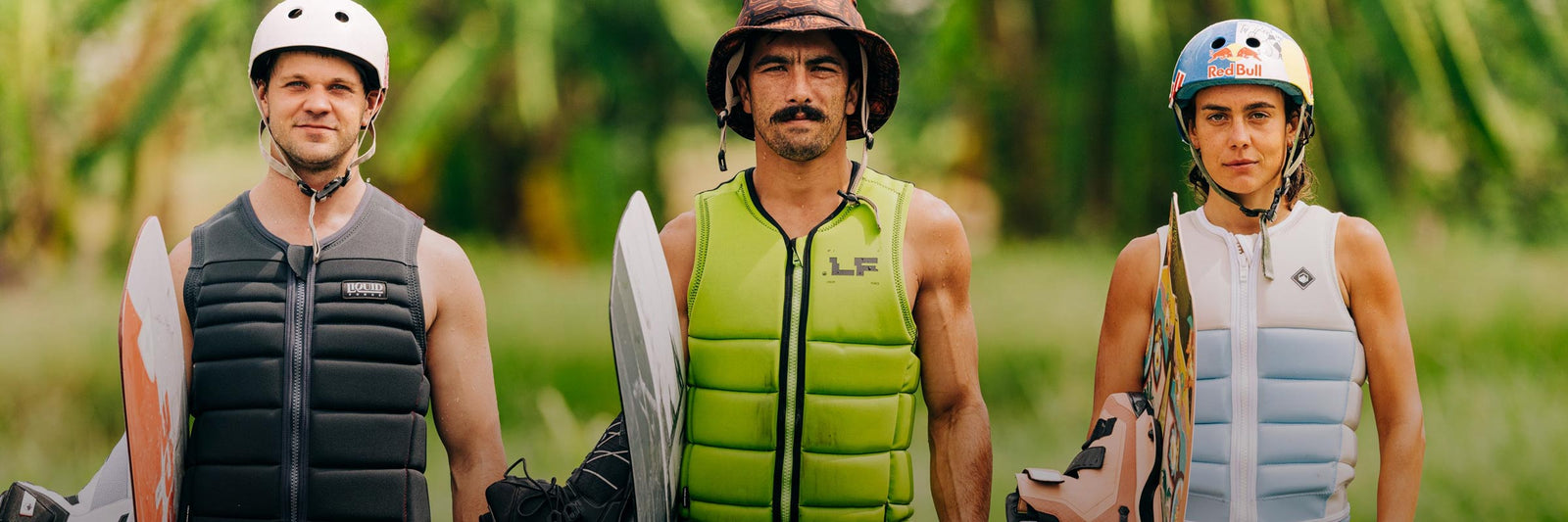 Three riders in comp vests and helmets stand side by side holding wakeboards.