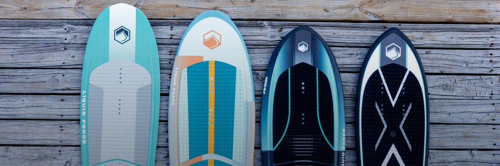 Four wakesurf and foil boards arranged upright on a weathered wooden dock.