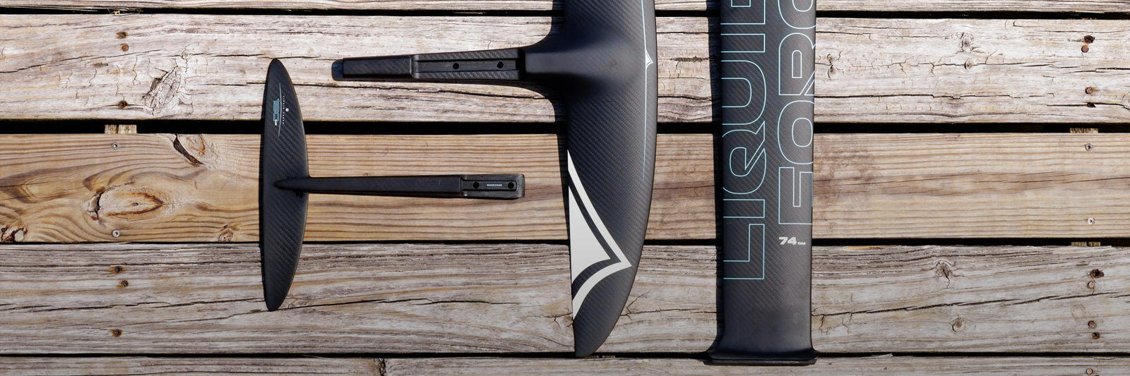 Close-up of carbon foil components arranged on a weathered wooden dock in daylight.