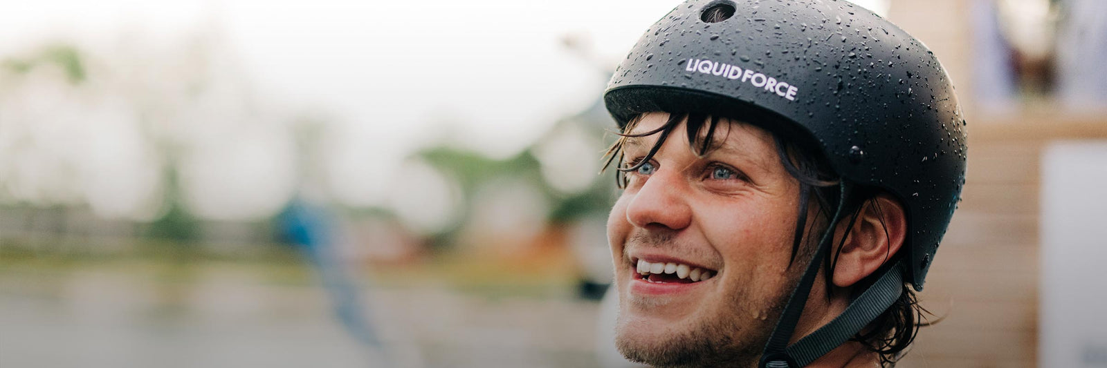 Smiling rider wearing a black Liquid Force helmet with water droplets on the surface.