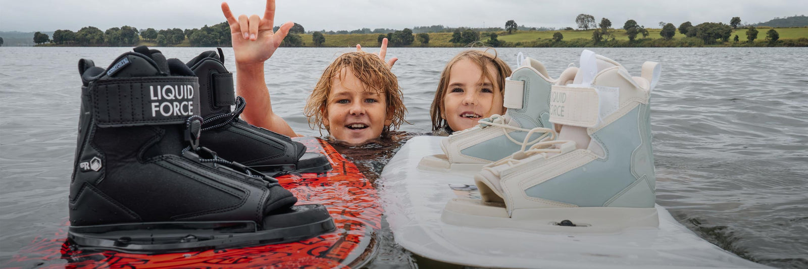 Two kids in the water holding wakeboards with boots attached.