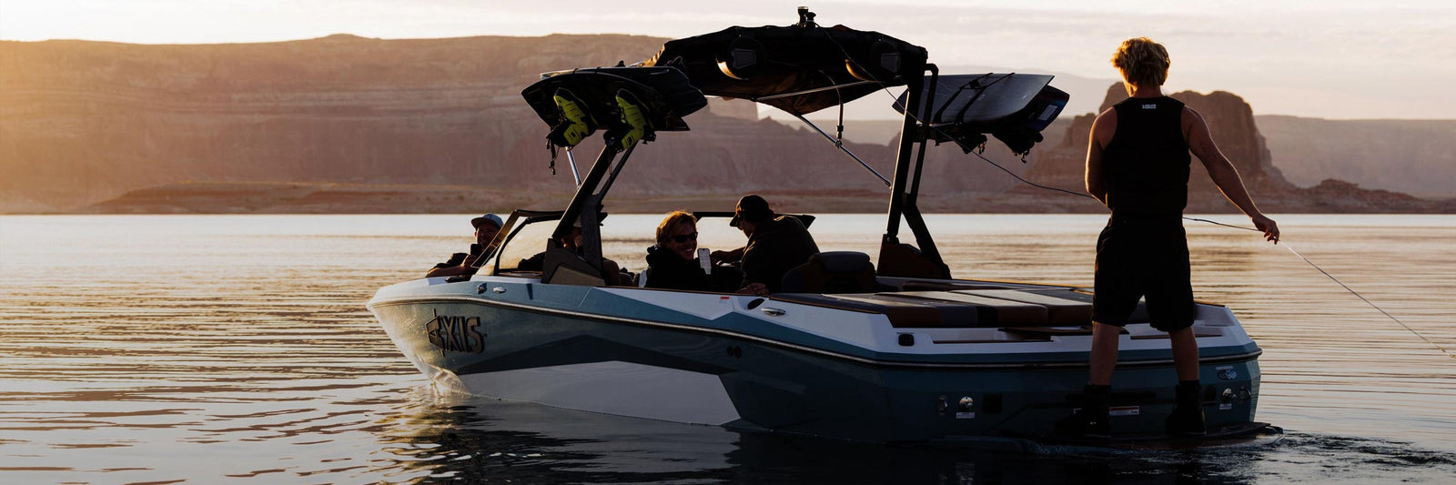 Riders relax on a boat at sunset as one stands holding a tow rope.