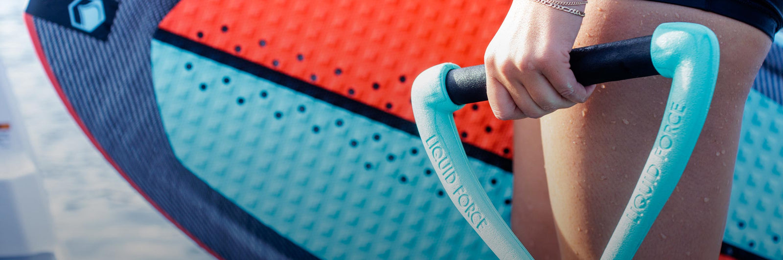 Rider grips a teal handle with a wakesurf board visible in the background.