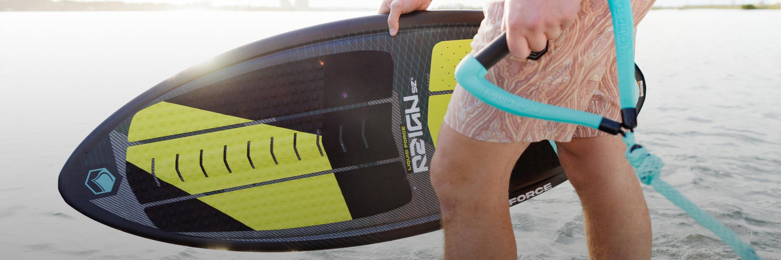 Rider holds a skim-style board and rope handle while standing ankle-deep in water.