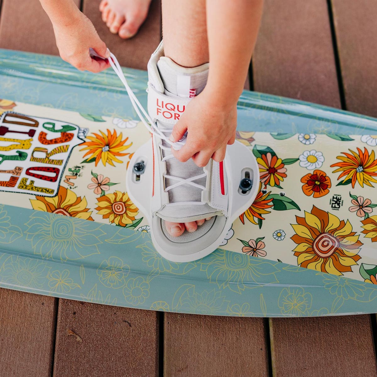 Liquid Force Kids Wakeboard Package - Closeup shot of younger rider lacing up her bindings on her wakeboard setup.