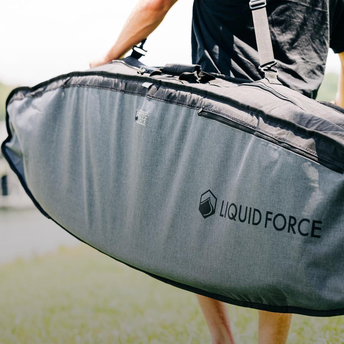 Person carries a large padded board bag with the Liquid Force logo on the side.