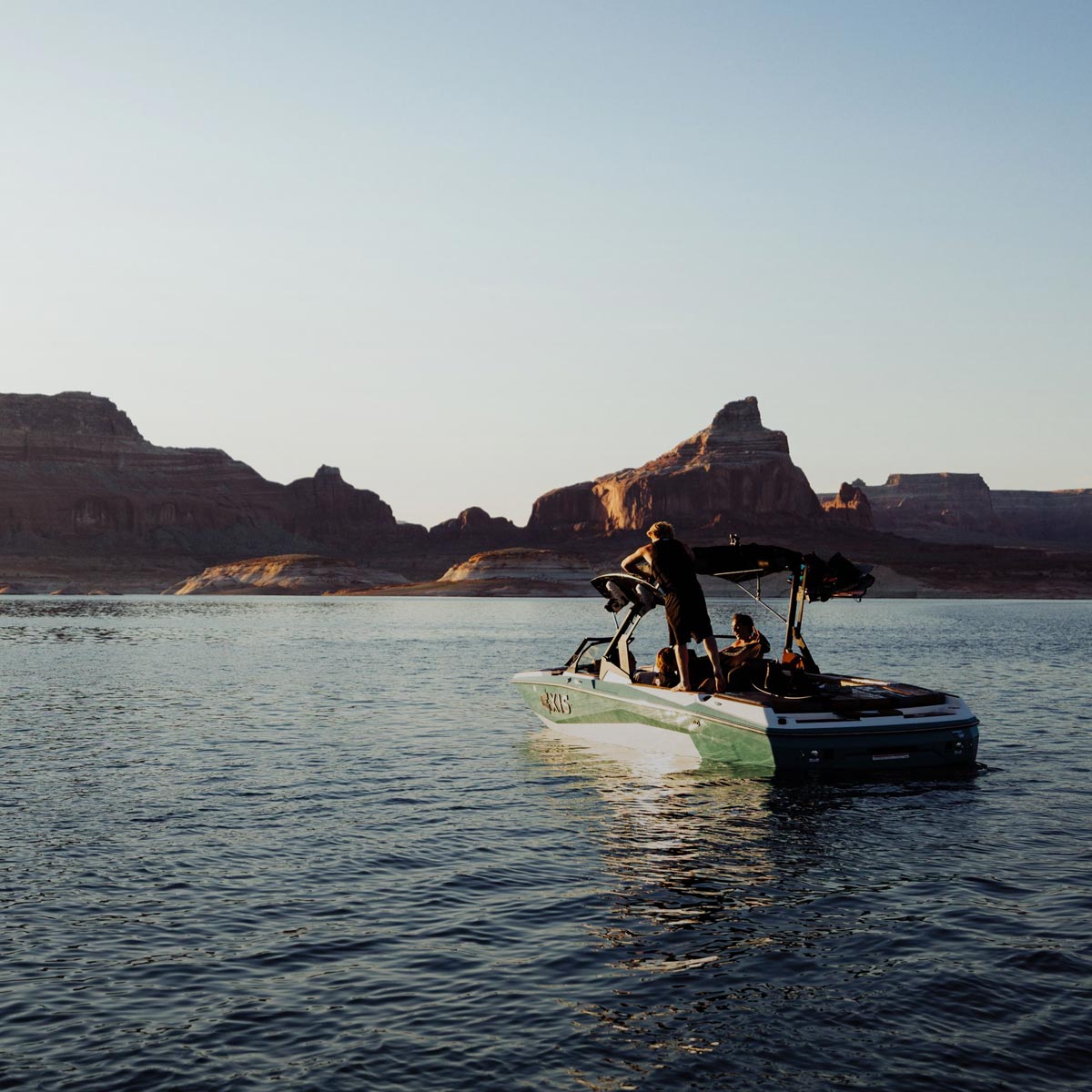Boat with riders floats on a calm lake with large rocky cliffs in the background.