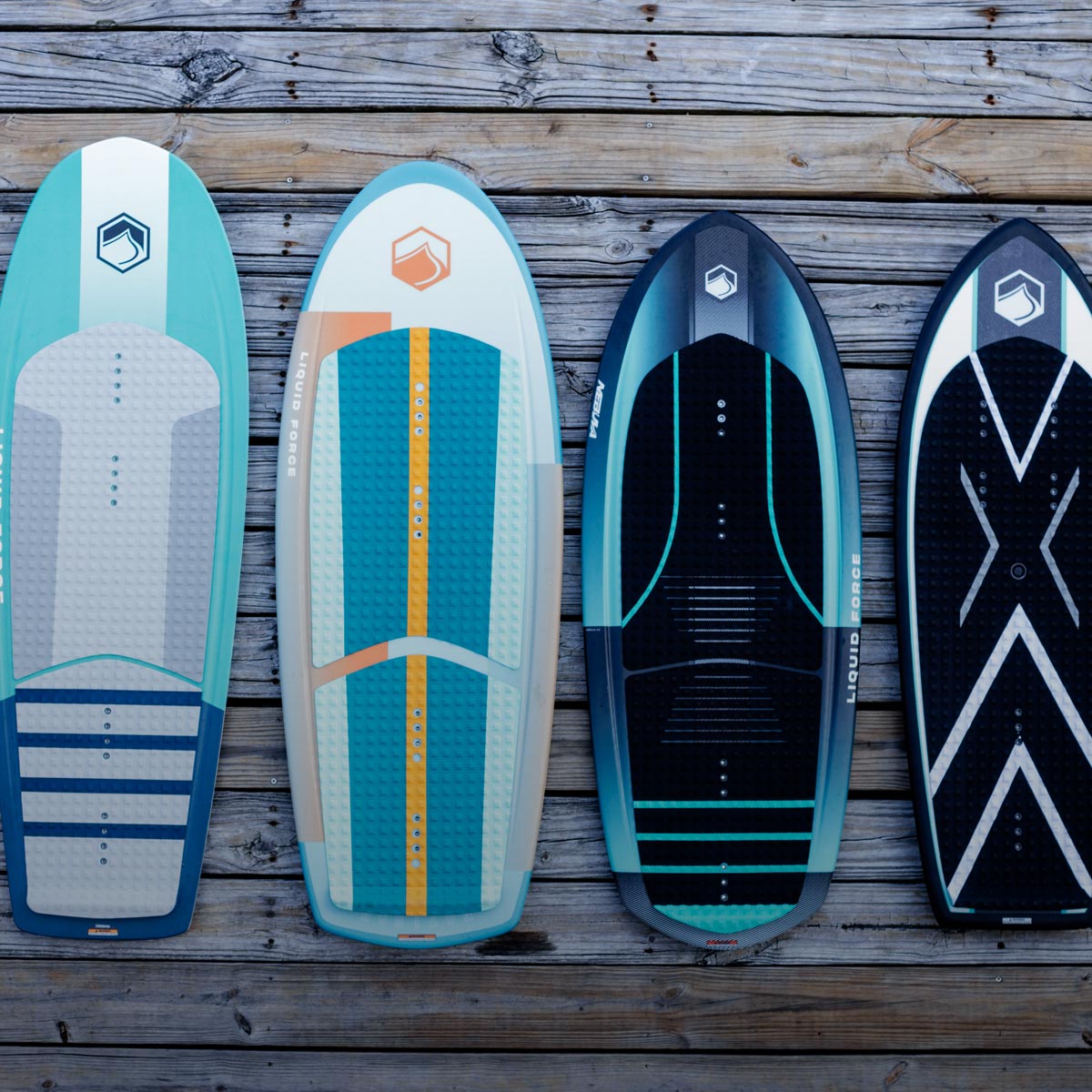 Four wakesurf and foil boards arranged upright on a weathered wooden dock.