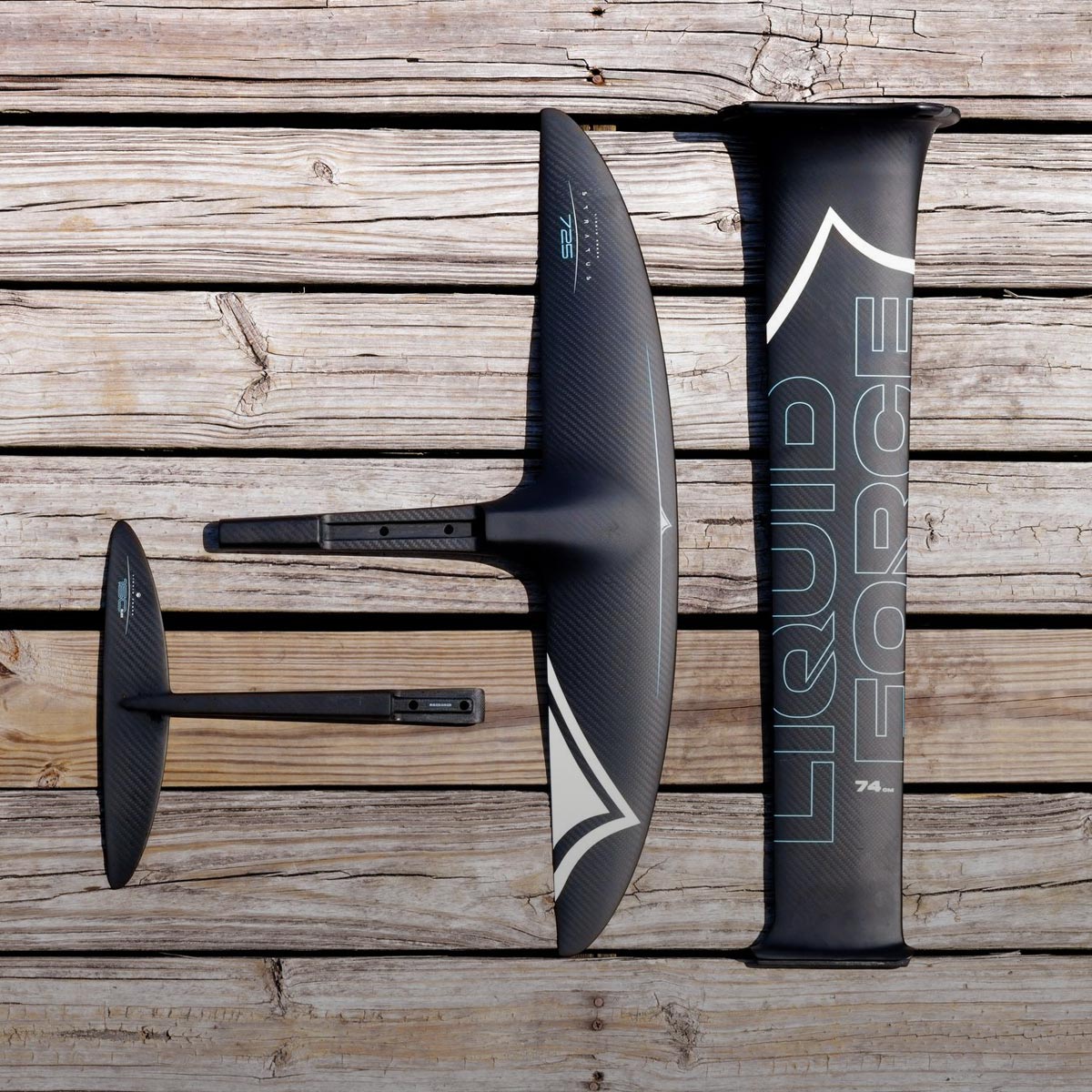 Close-up of carbon foil components arranged on a weathered wooden dock in daylight.