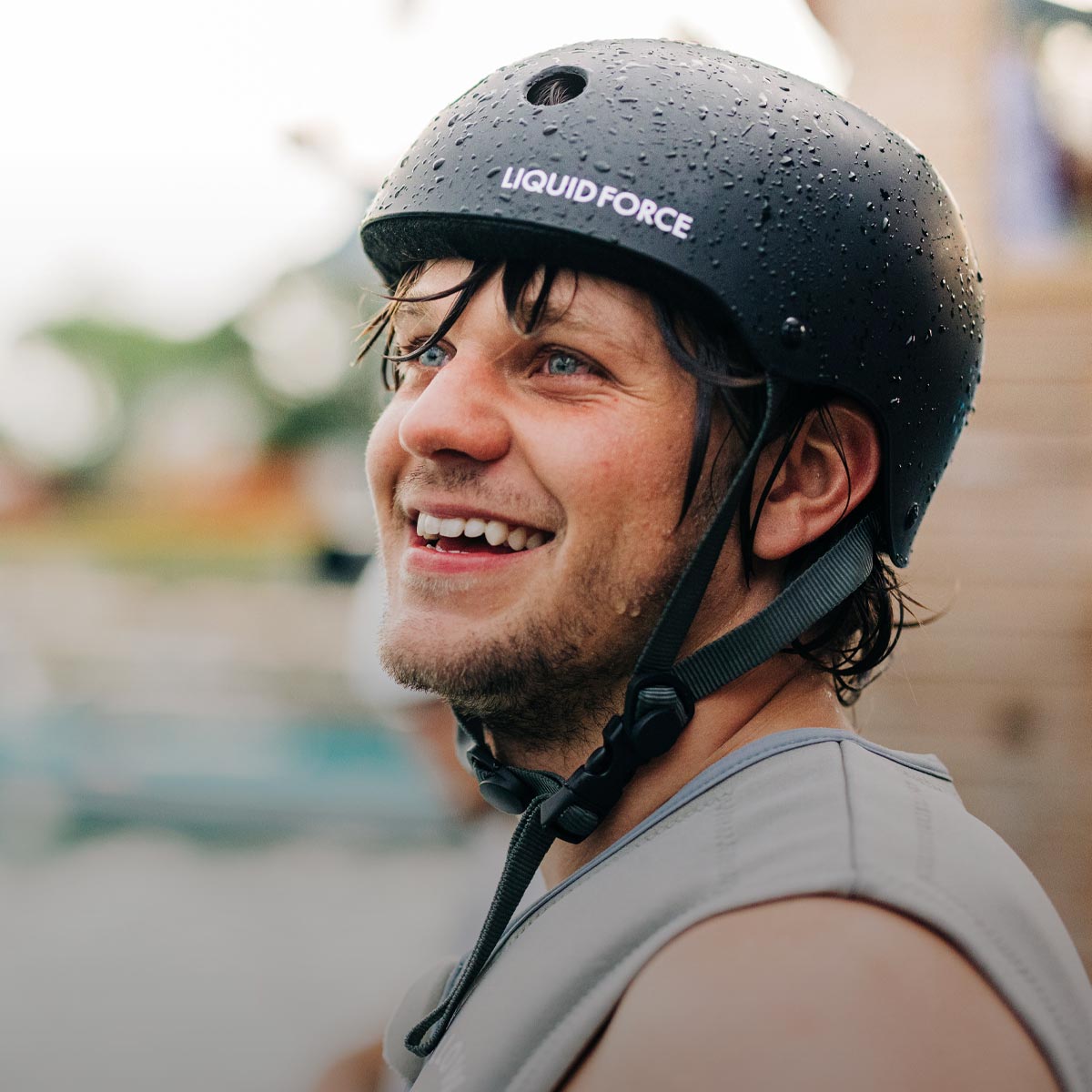 Smiling rider wearing a black Liquid Force helmet with water droplets on the surface.