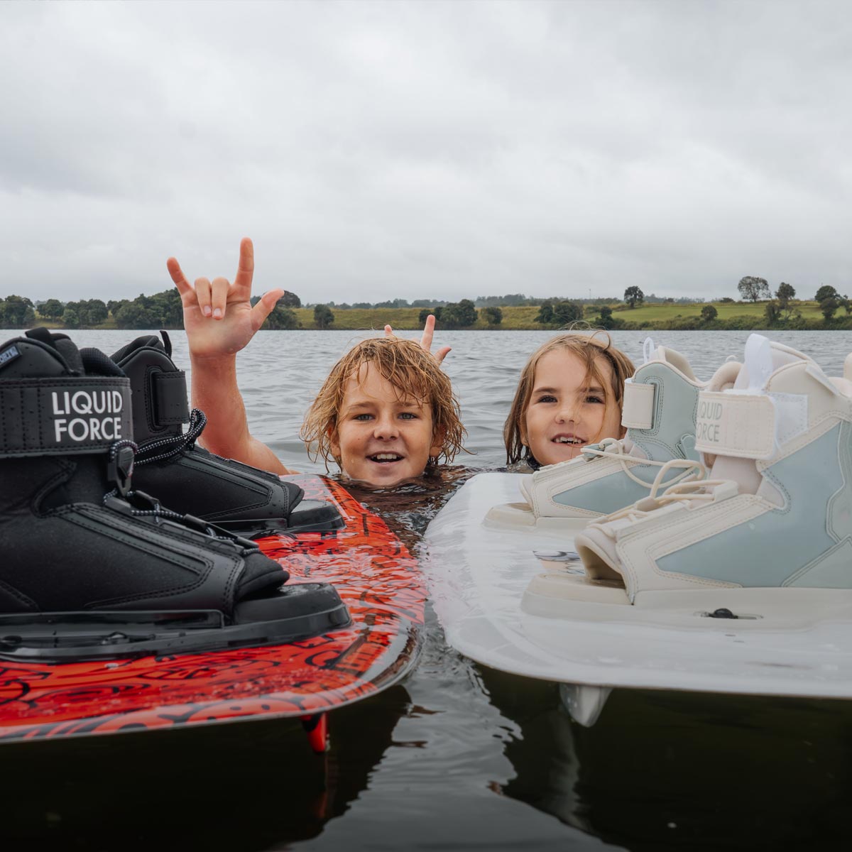 Two kids in the water holding wakeboards with boots attached.