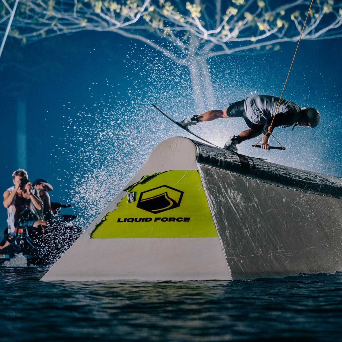 Rider grinding a wake park feature at night with water spraying around.