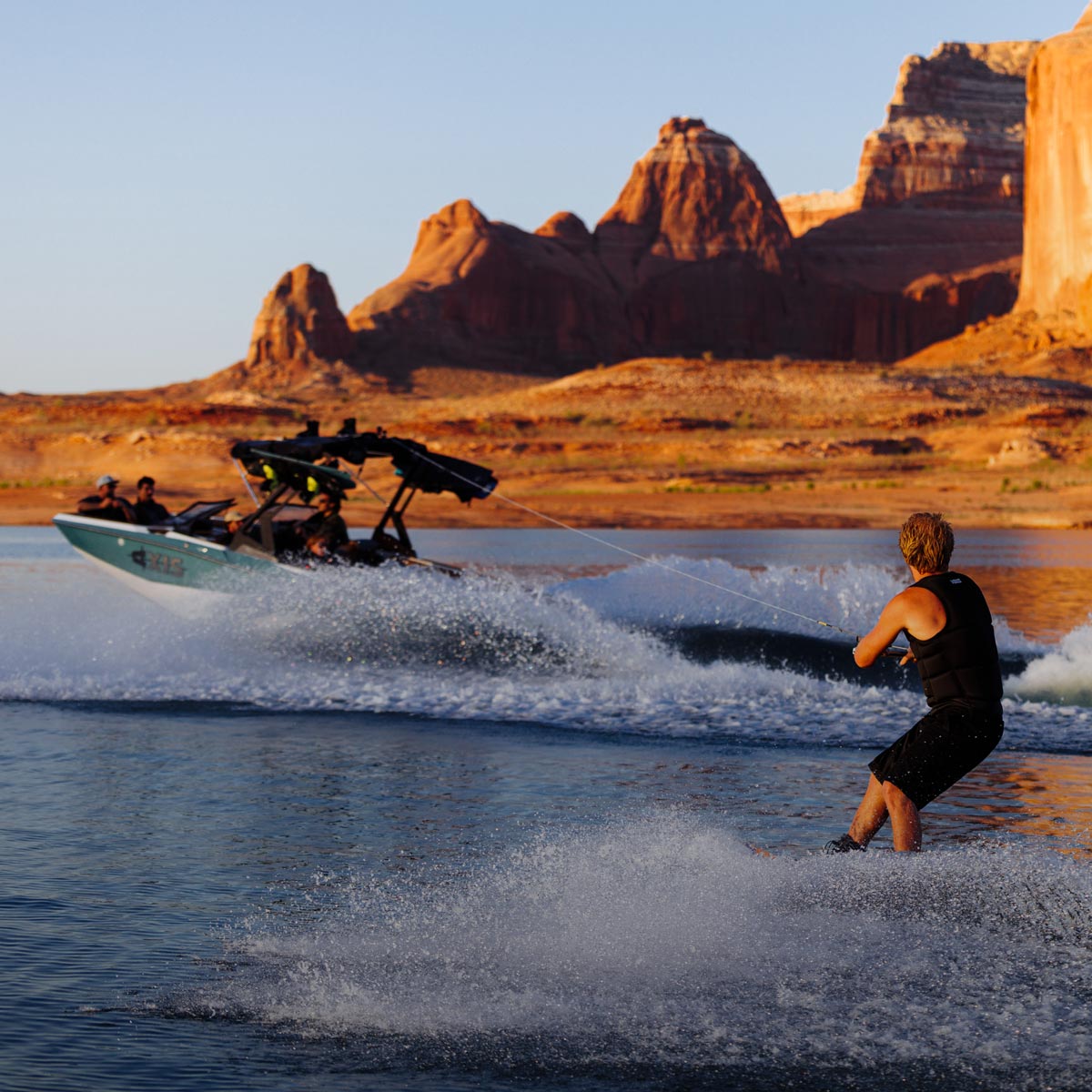 Wakeboarder carving behind a boat on a scenic desert lake at sunset.