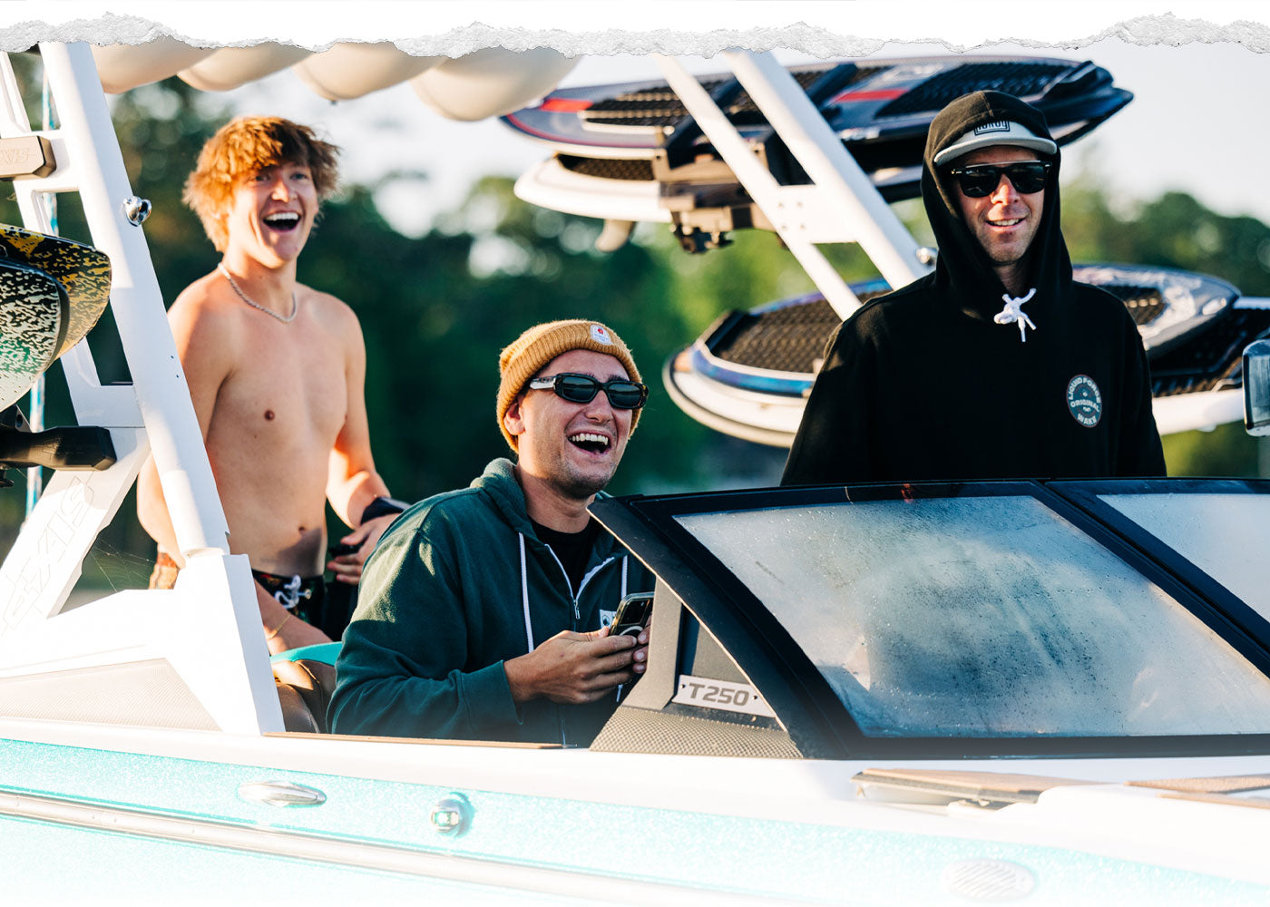 Group of men smiling and laughing on a boat with wakeboards attached.