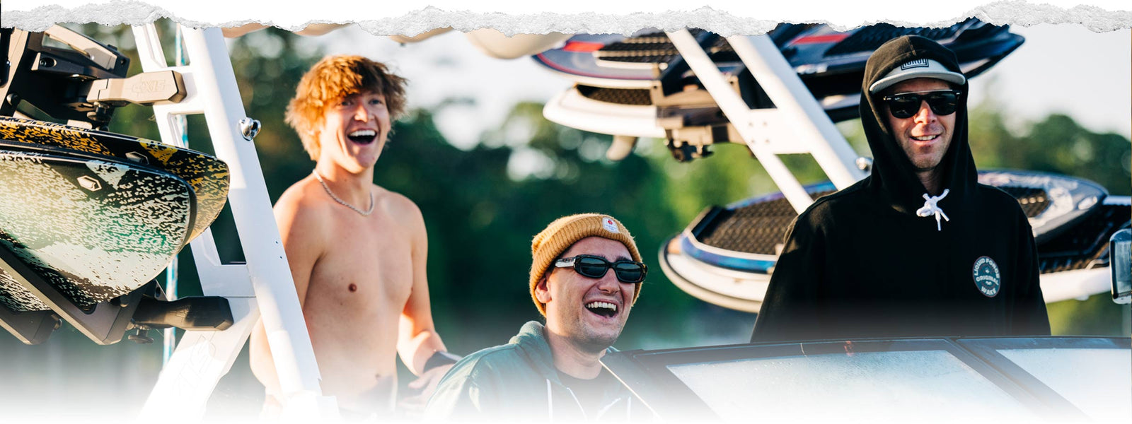 Group of men smiling and laughing on a boat with wakeboards attached.